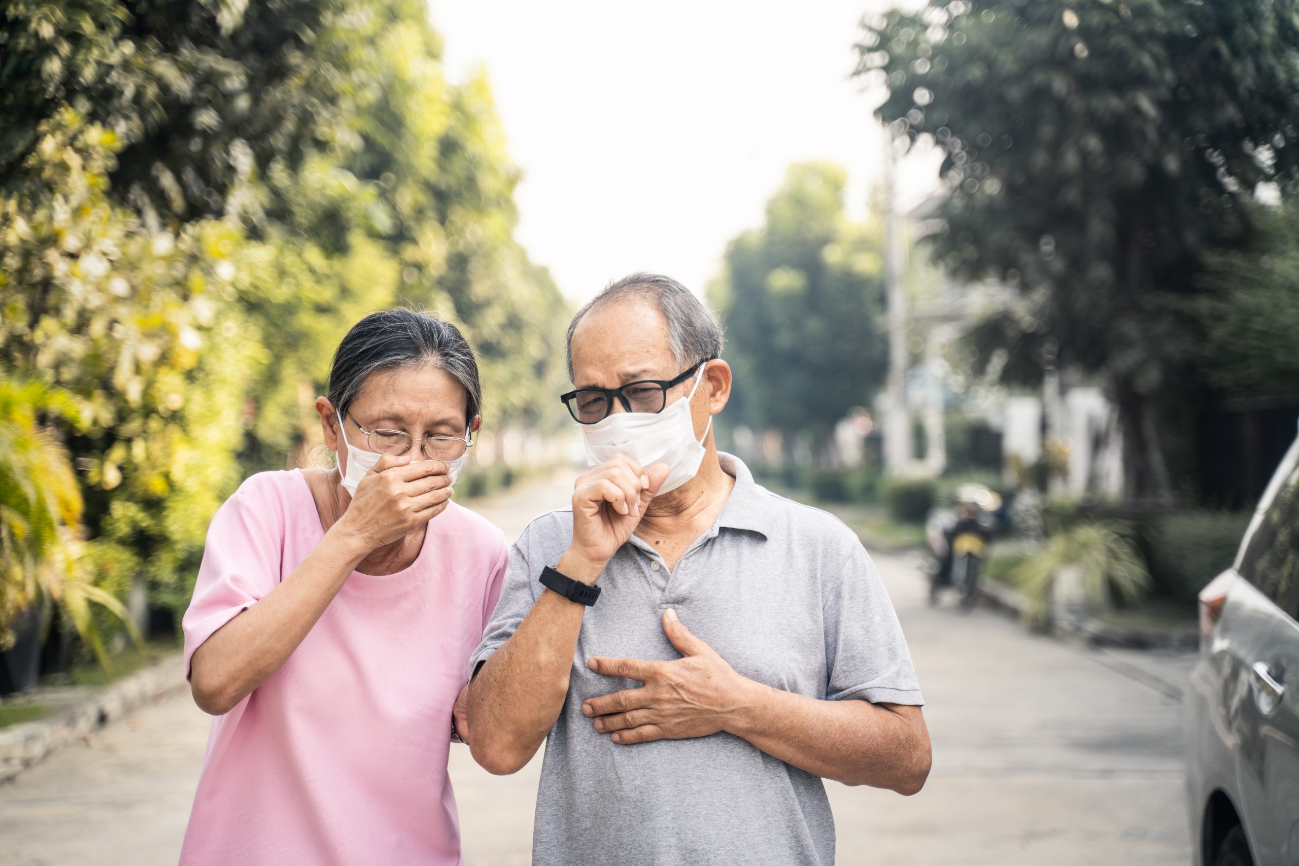 Asian elder senior couple wearing mask for prevent dusk pm 2.5 bad air pollution. Old woman and man holding mask and having a cough due to bad smell and allergic sickness symptom stand on street.